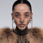 Portrait of female middle eastern AI model with silver piercings in nose area, ears and chin. Face covered by brown animal pattern face paint. Fur coat. AI fashion editorial.